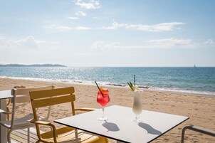 Una mesa en la playa con dos bebidas y vistas al mar.