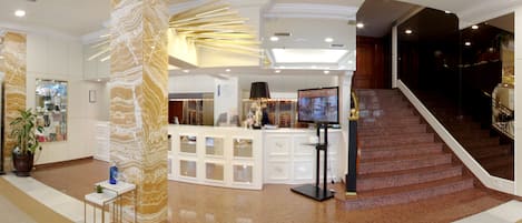 A lobby with a reception desk, a TV, a staircase, and a potted plant.