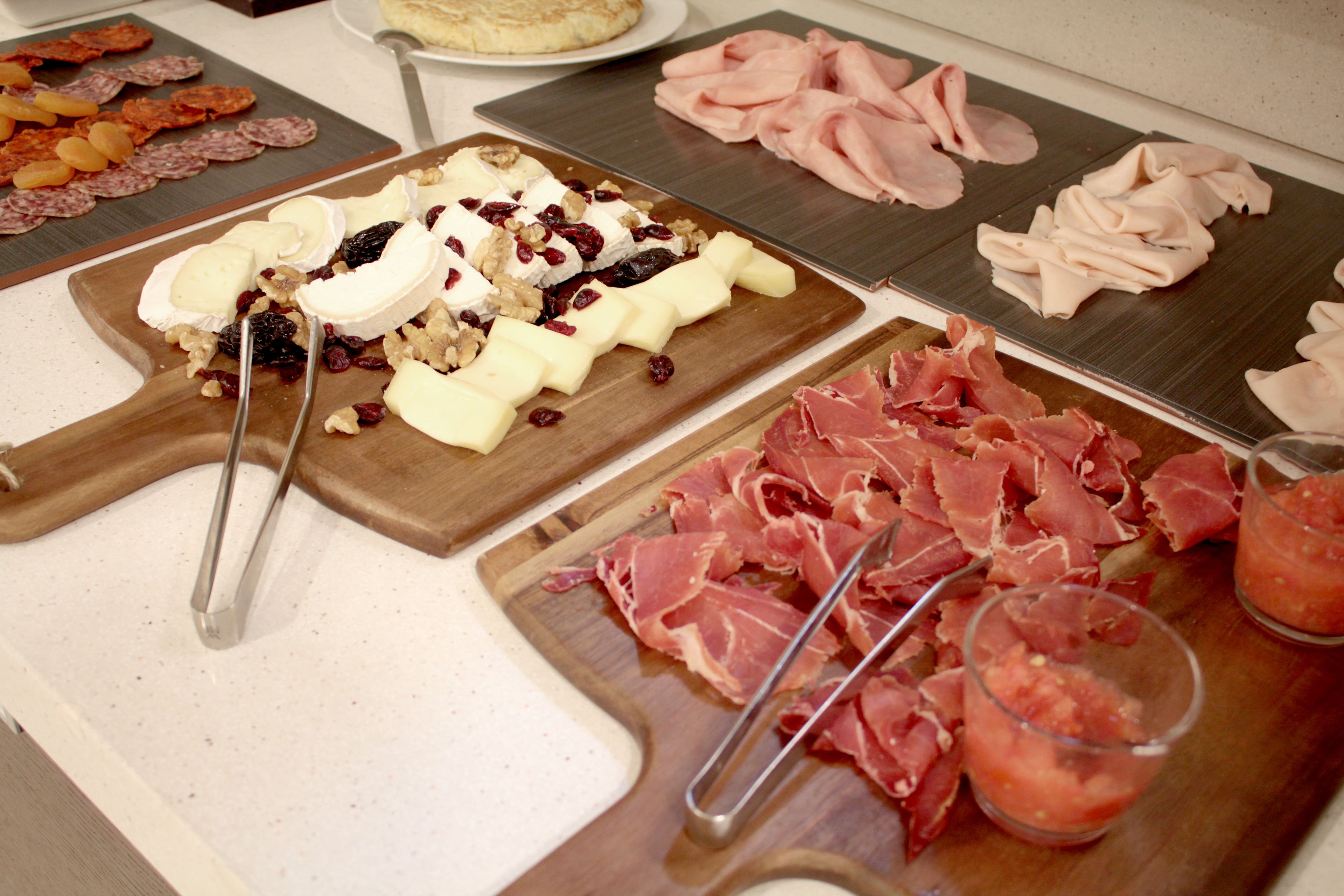 A buffet with various cheeses, meats, and fruits.