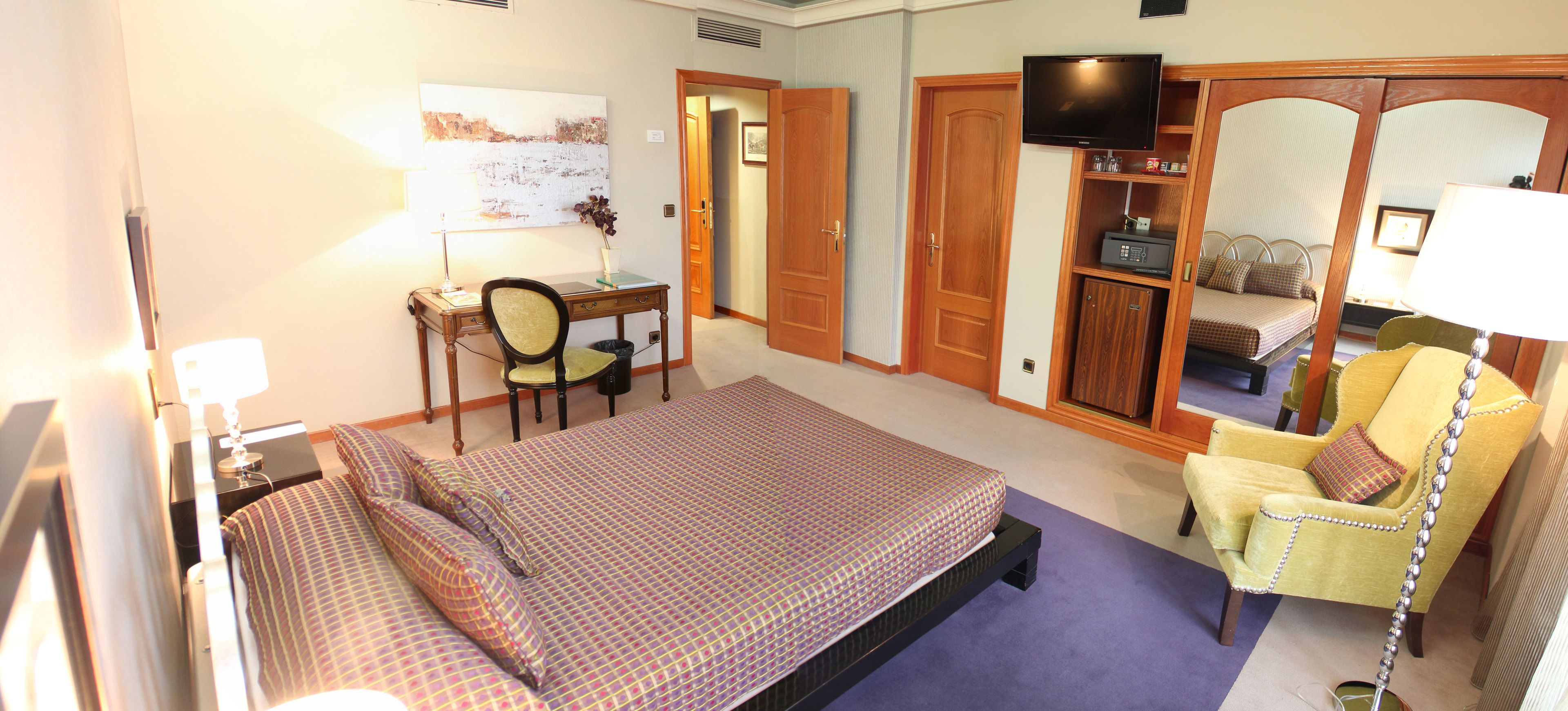 Habitación de hotel con cama, escritorio, silla, televisor y armario.