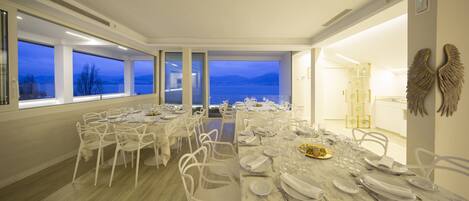 Comedor con vista a un lago y montañas, sillas blancas y una mesa lista para una comida.