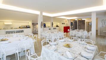 A spacious dining area with multiple round tables set for a meal, surrounded by white chairs.