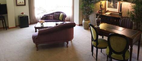 A living room with a sofa, a coffee table, a dining table with chairs, a television, and framed pictures on the wall.