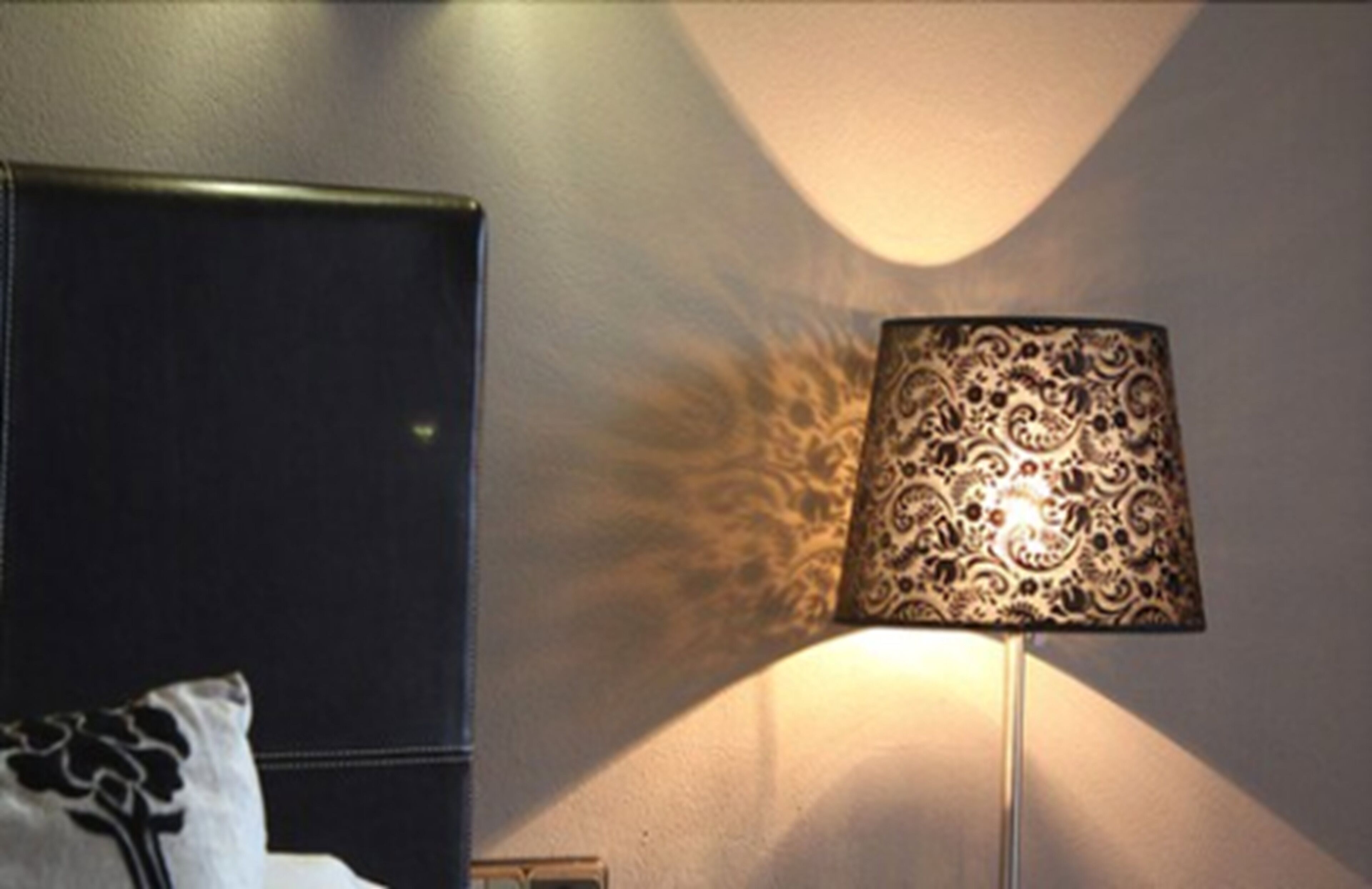 Ein Zimmer mit einem Bett, einer strukturierten Lampe und einer Wand mit einer dekorativen Leuchte.