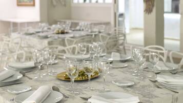A dining area with tables set for a meal, featuring white chairs and a floral tablecloth.