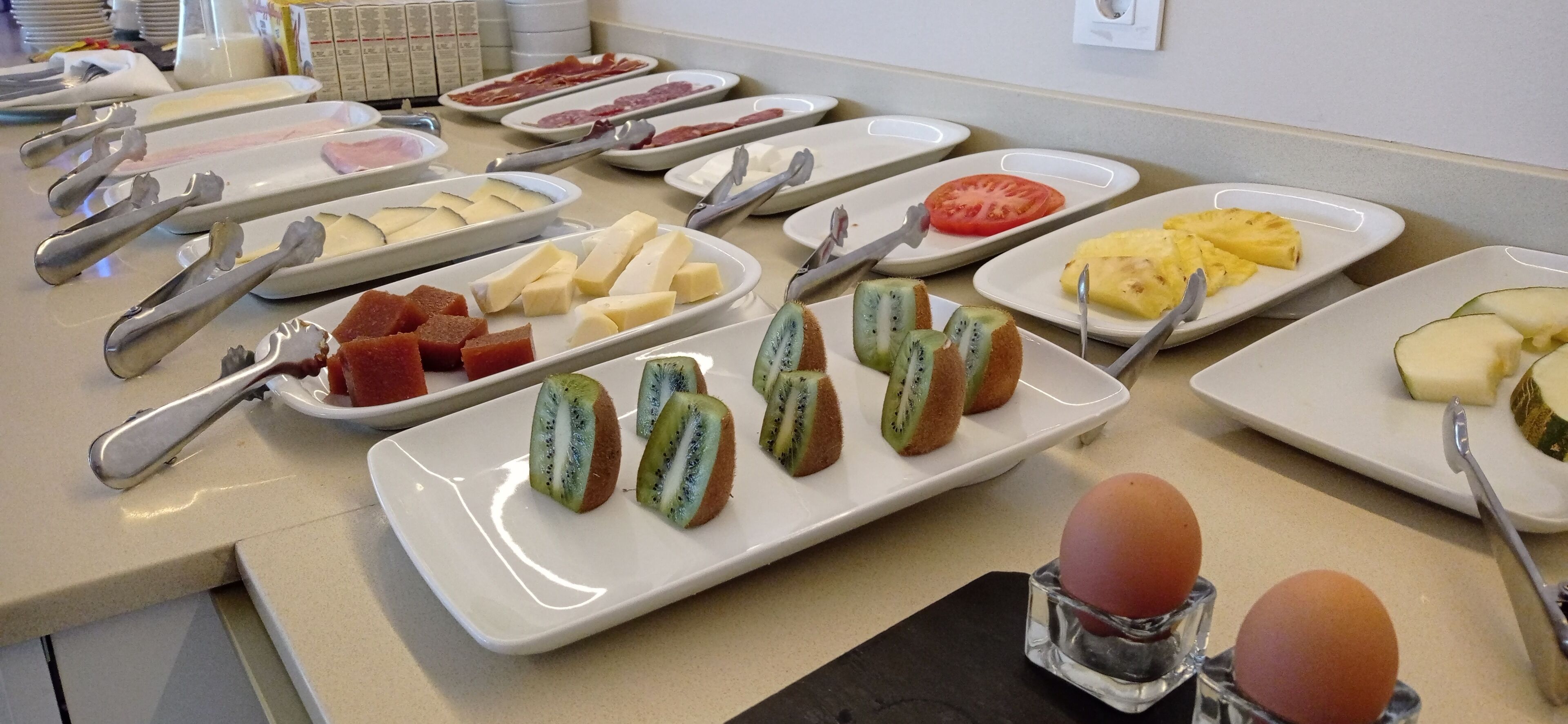 Un bufé con distintos alimentos, entre ellos queso, carnes, frutas y huevos.