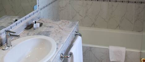 Un baño con lavamanos de mármol, un espejo grande, una bañera y una zona de ducha.