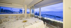 A dining area with tables set for a meal, large windows offering a view of a marina and cityscape. - Hotel Ciudad de Vigo (Vigo)
