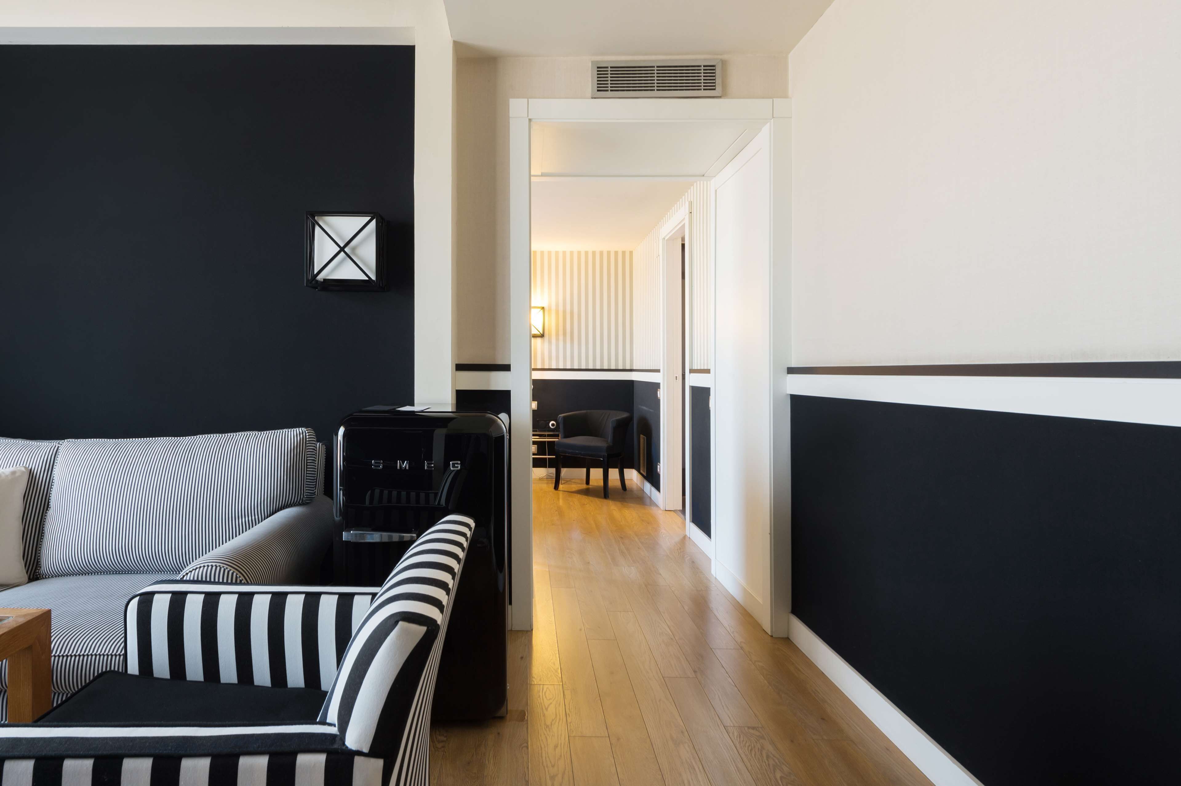 A modern living room with a black and white striped sofa, a black armchair, and a black gaming console.