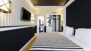 Habitación de hotel con pared a rayas, una cama grande con ropa de cama blanca y negra, un televisor de pantalla plana montado en la pared y un vestidor con espejo y ropa colgada.