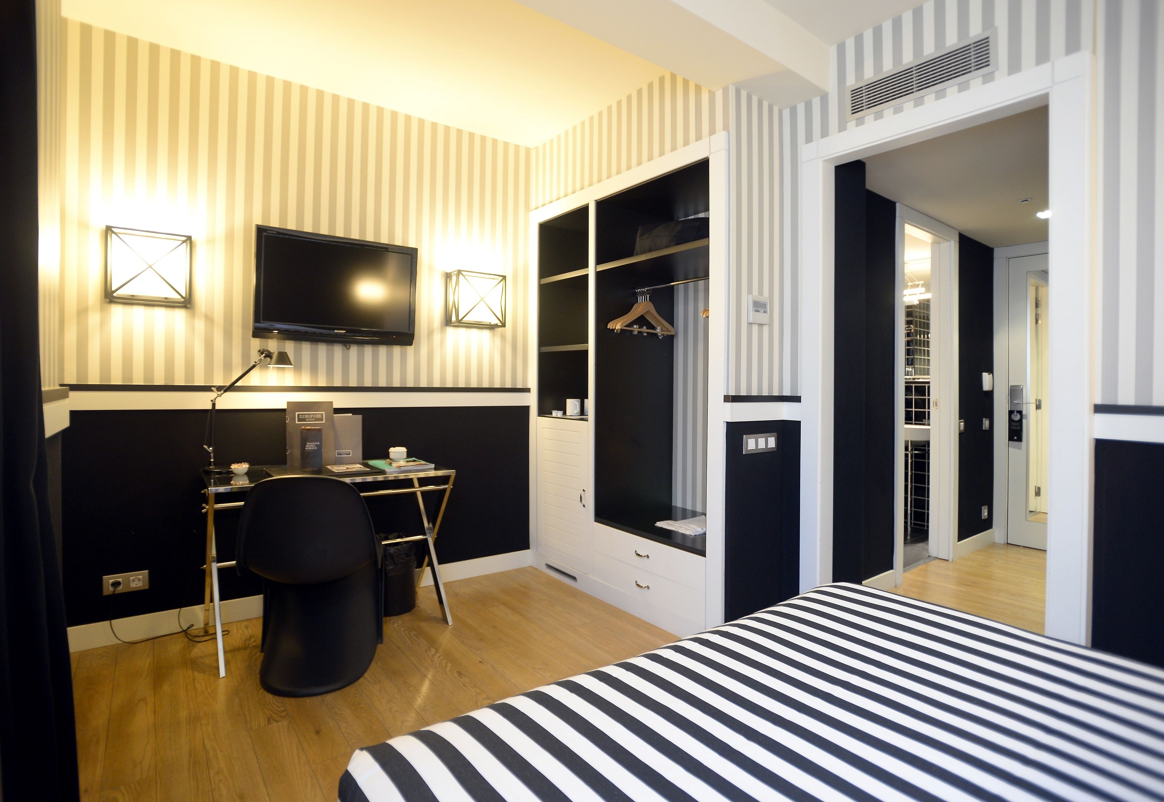 A hotel room with a bed, desk, chair, TV, wardrobe, and a mirror.