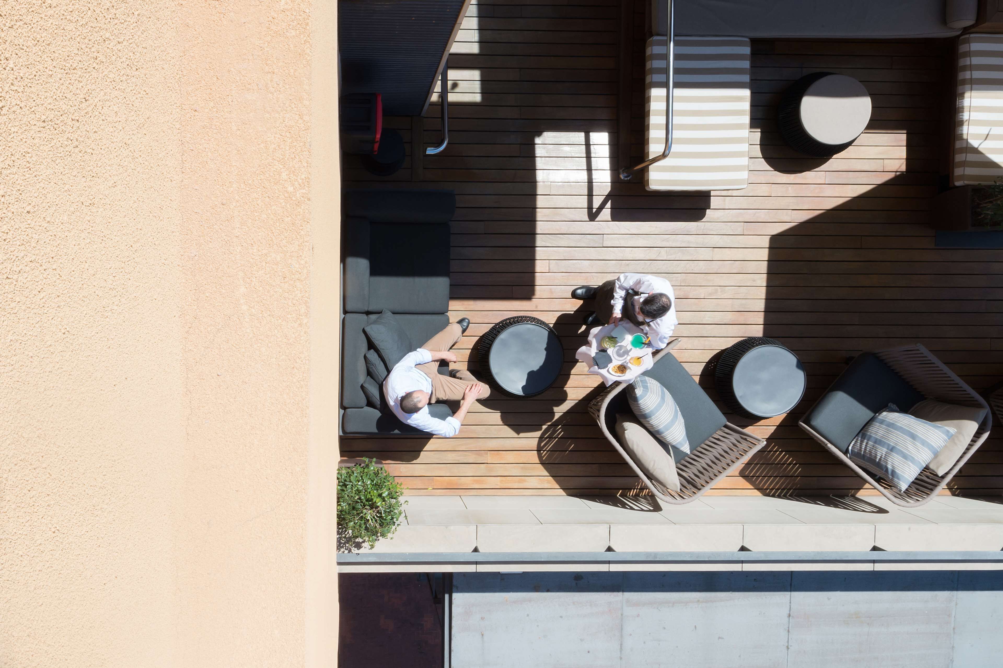 Una terraza en la azotea con piso de madera, una mesa redonda y dos sillones con cojines.