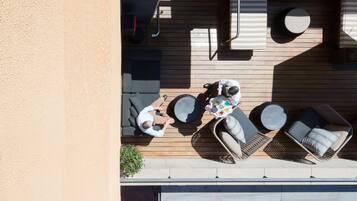 Una terraza en la azotea con piso de madera, una mesa redonda y dos sillones con cojines.