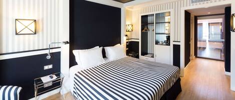 A modern hotel room with a large bed, a seating area with a chair, a small table, and a wardrobe.