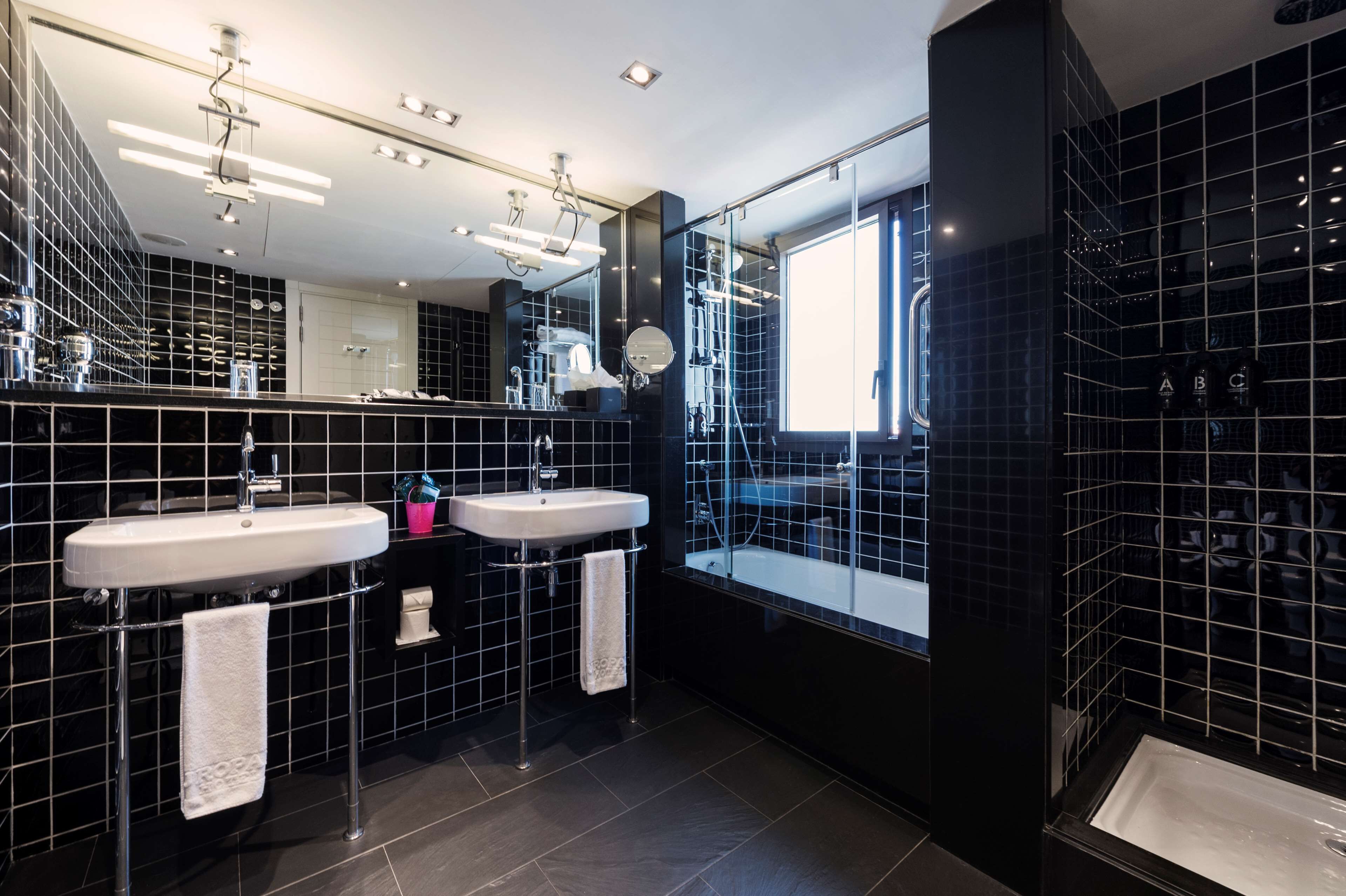A modern bathroom with two sinks, a large mirror, and a bathtub.