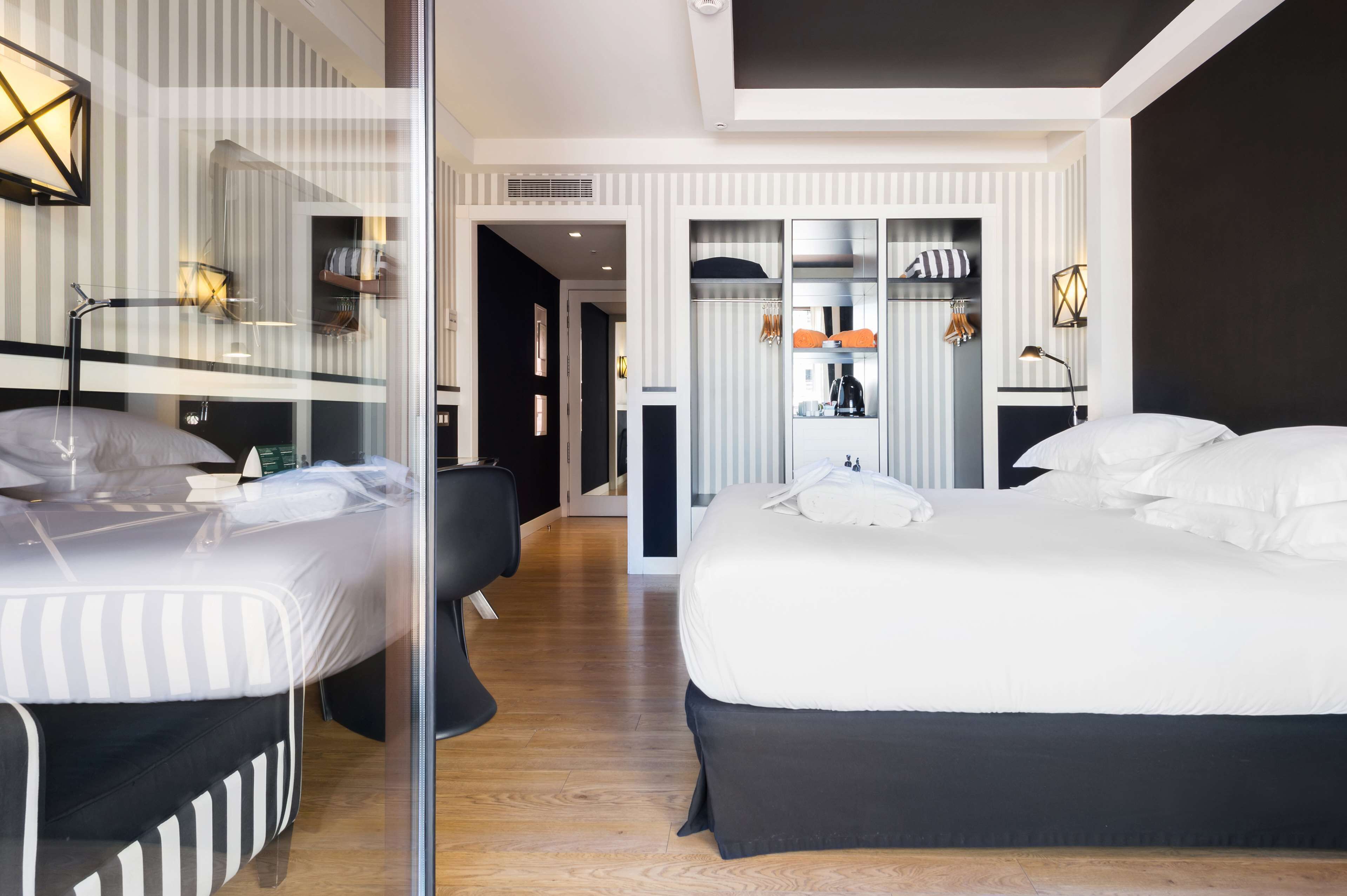 A modern hotel room with a large bed, a separate seating area, and a view into the hallway.
