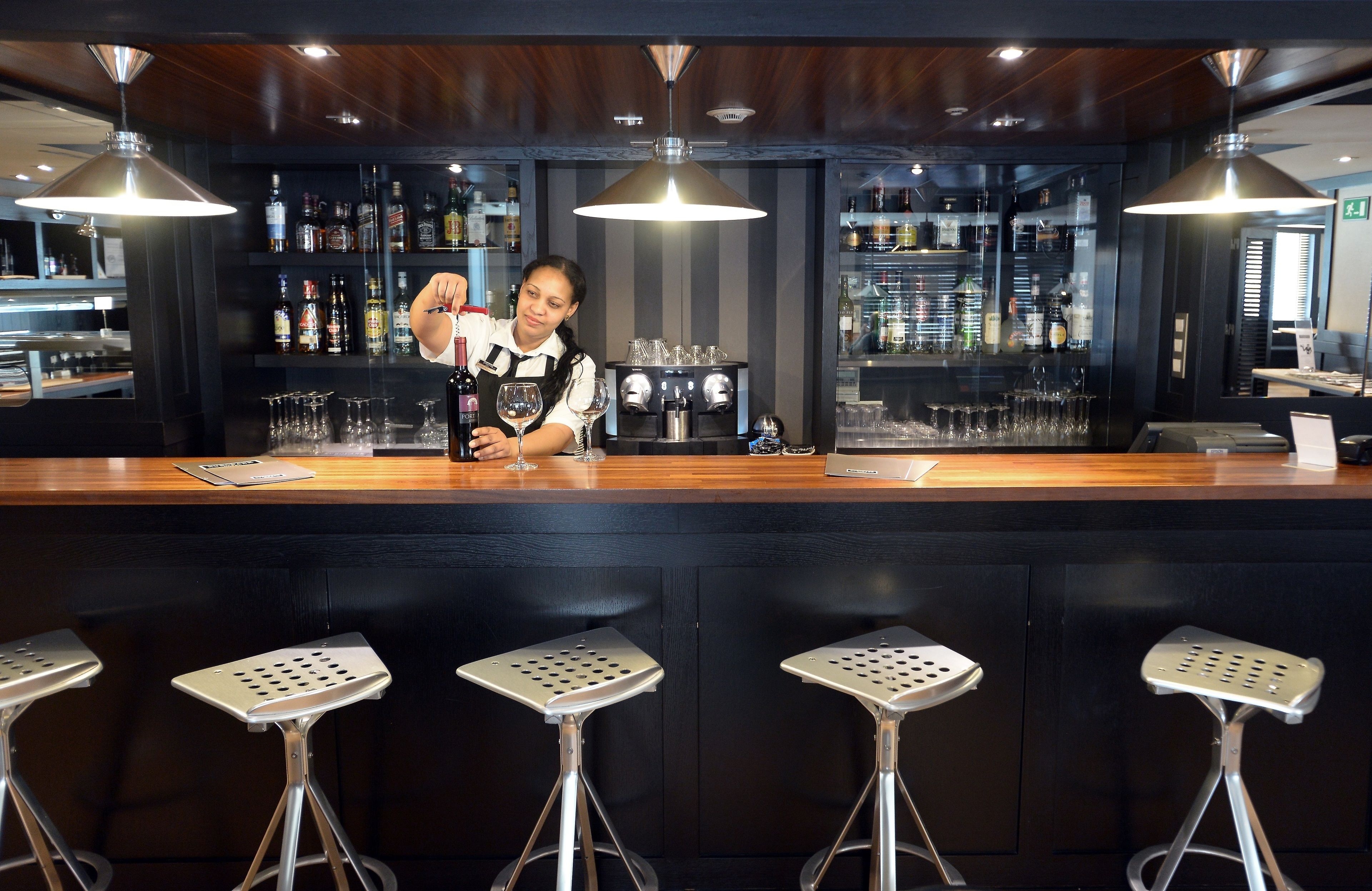 A bar area with a bartender, bar stools, and shelves of liquor bottles.