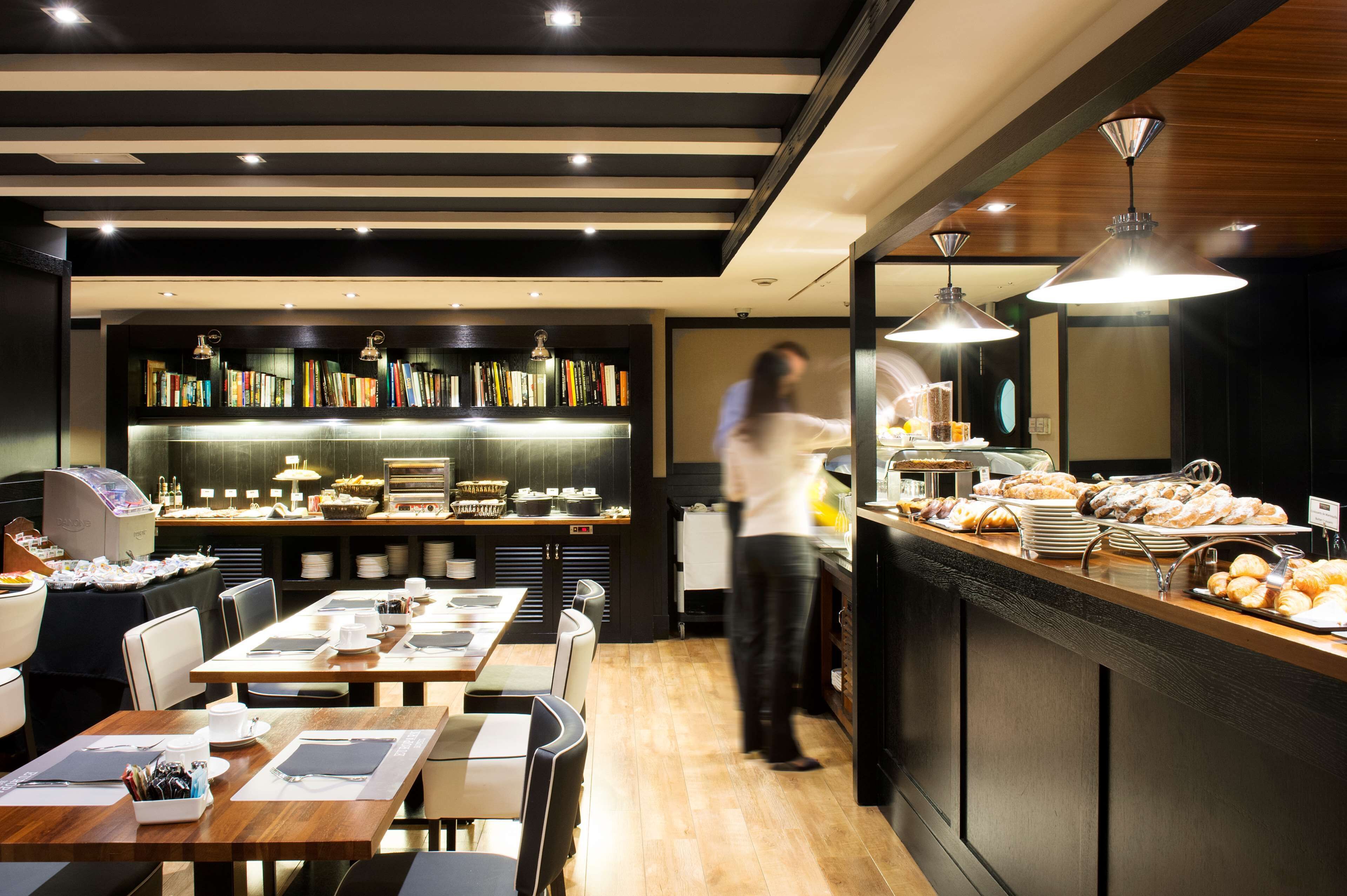A modern restaurant with a long counter, a bookshelf, and a buffet area.