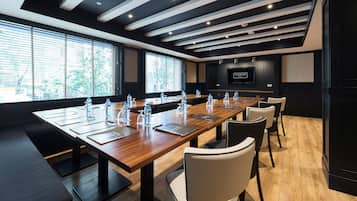 Sala de conferência com uma mesa comprida, cadeiras, garrafas de água e uma tela de TV.