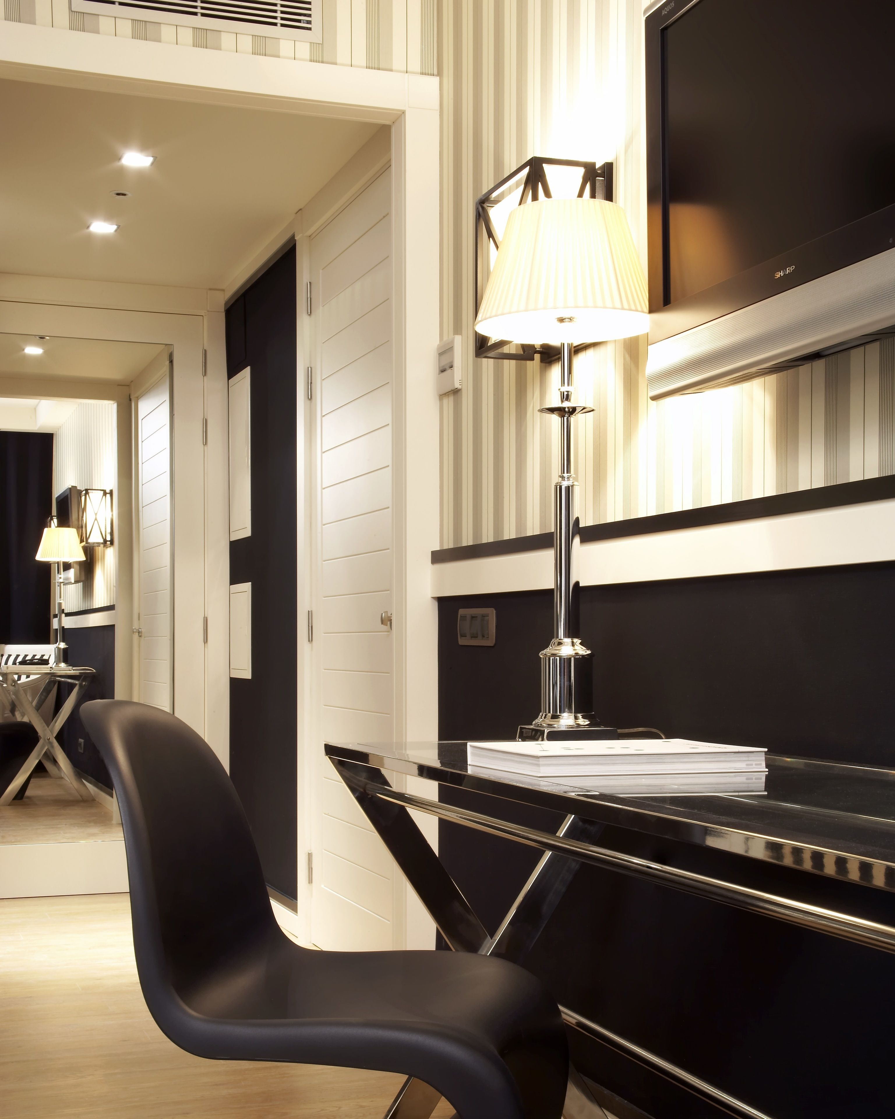 Une chambre d’hôtel moderne avec un bureau noir, une lampe, une télévision et une chaise.