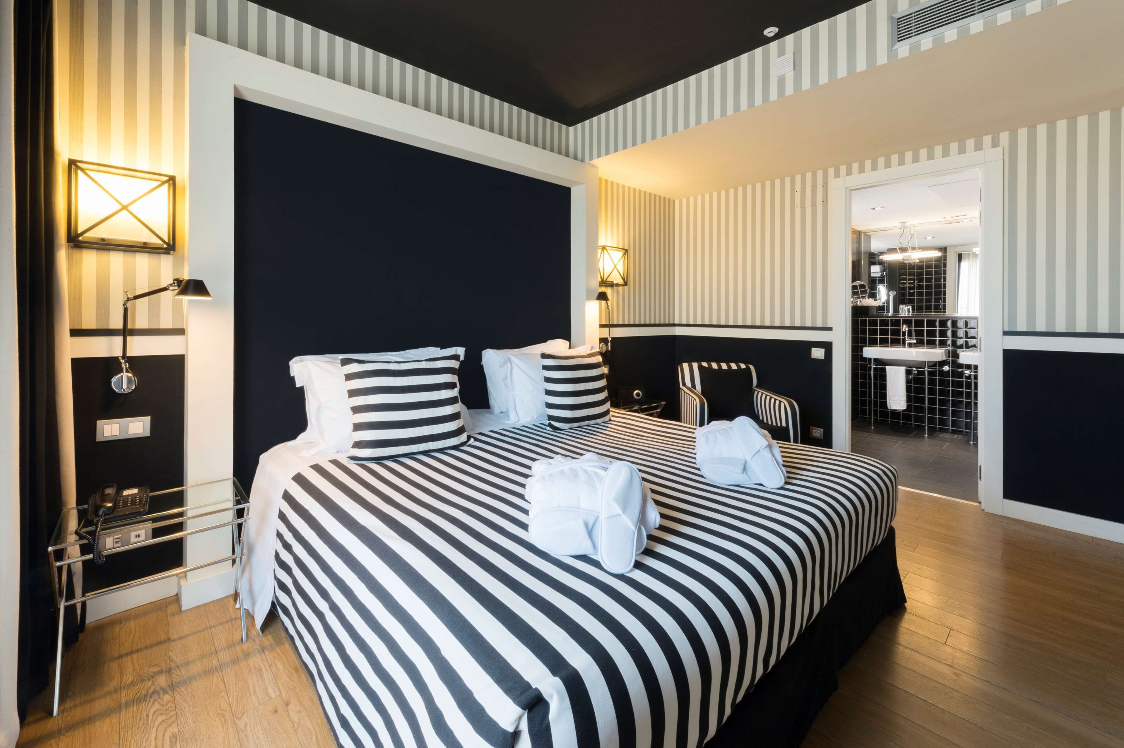 Habitación de hotel con una cama grande, mesitas de noche, un teléfono y un baño visible a través de una puerta abierta.