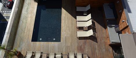 Un área de piscina en la azotea con terraza de madera, sillas de descanso y un sofá a cuadros.
