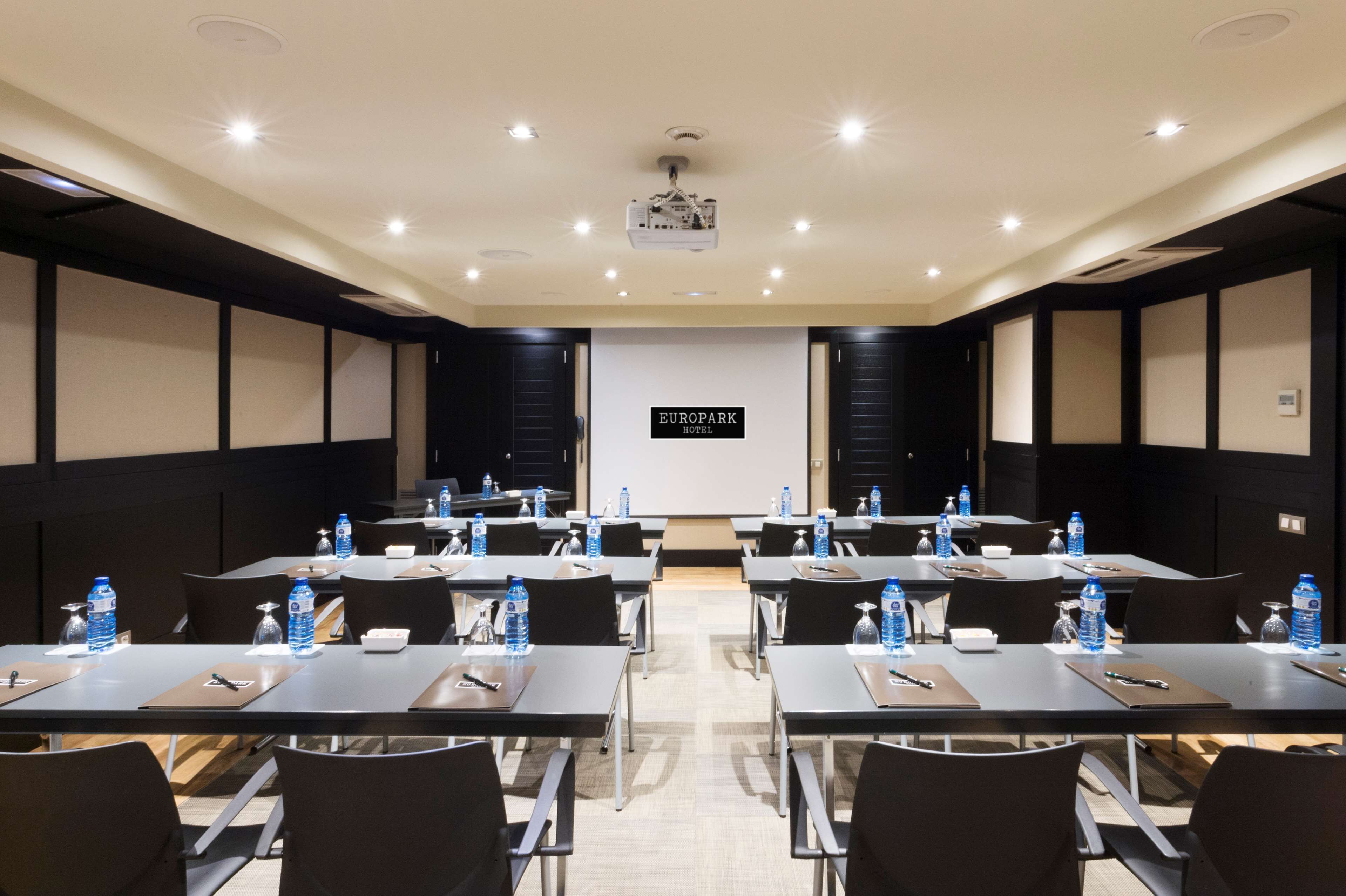 A conference room with tables, chairs, water bottles, and a projector screen.