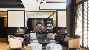 Una sala de estar moderna con un sofá negro, dos sillones y una mesa de centro. Se observan estanterías y una planta decorativa al fondo.