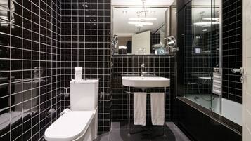 Un baño moderno con paredes de azulejos negros, un inodoro blanco, un lavabo y una zona de ducha con mampara de cristal.