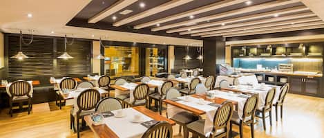 A restaurant with wooden tables and chairs, a modern ceiling design, and a bar area.