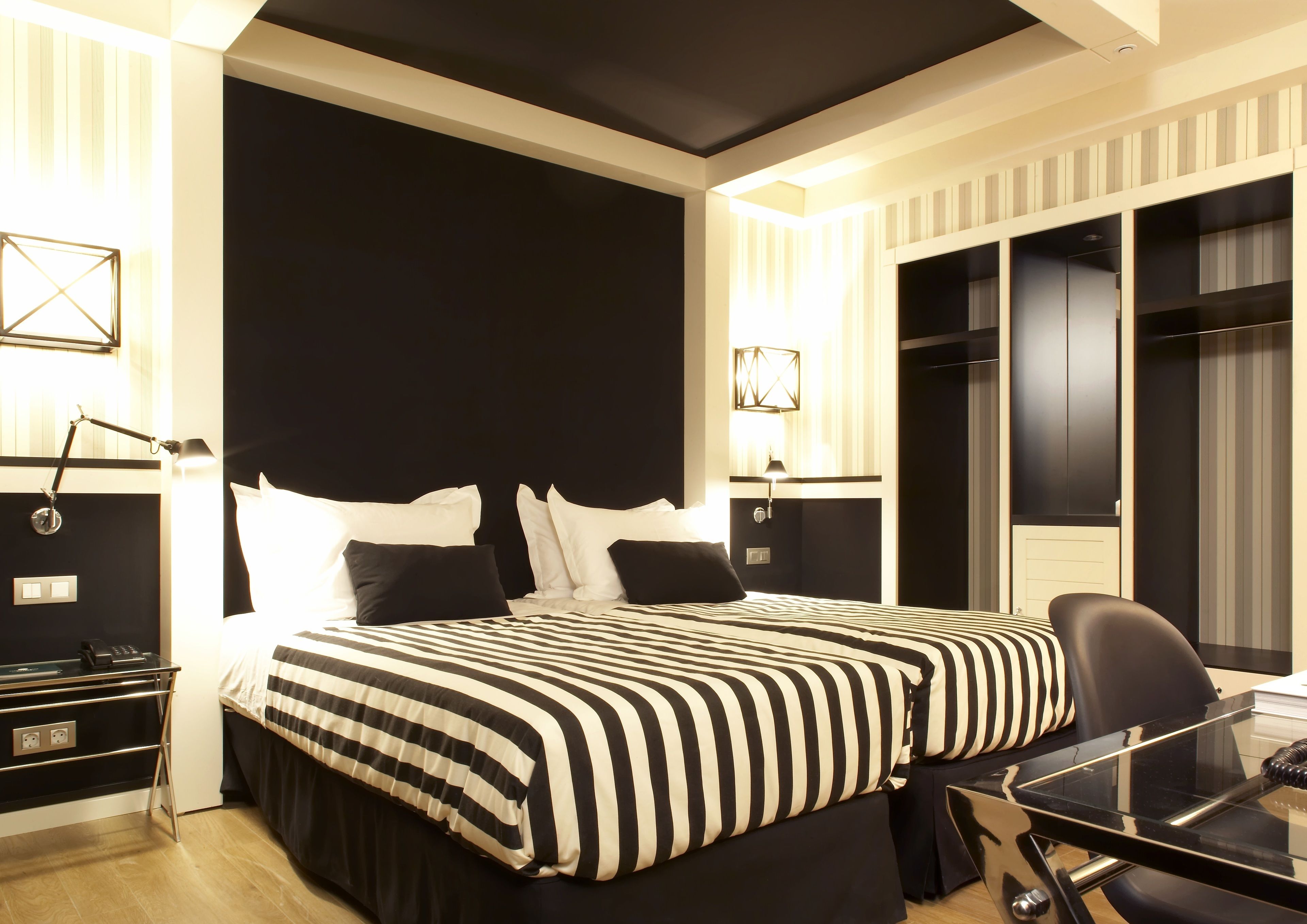 A modern hotel room with a large bed, a desk with a chair, and a wardrobe.