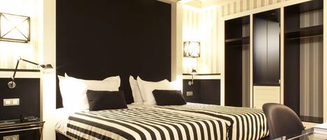 A modern hotel room with a large bed, a desk with a chair, and a wardrobe.