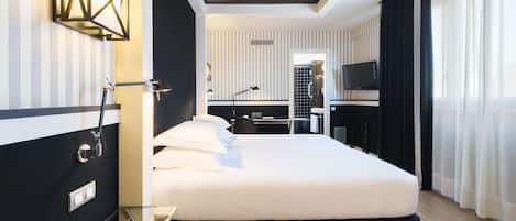 Una habitación de hotel moderna con una cama grande, un escritorio, un televisor y un baño con ducha e inodoro.