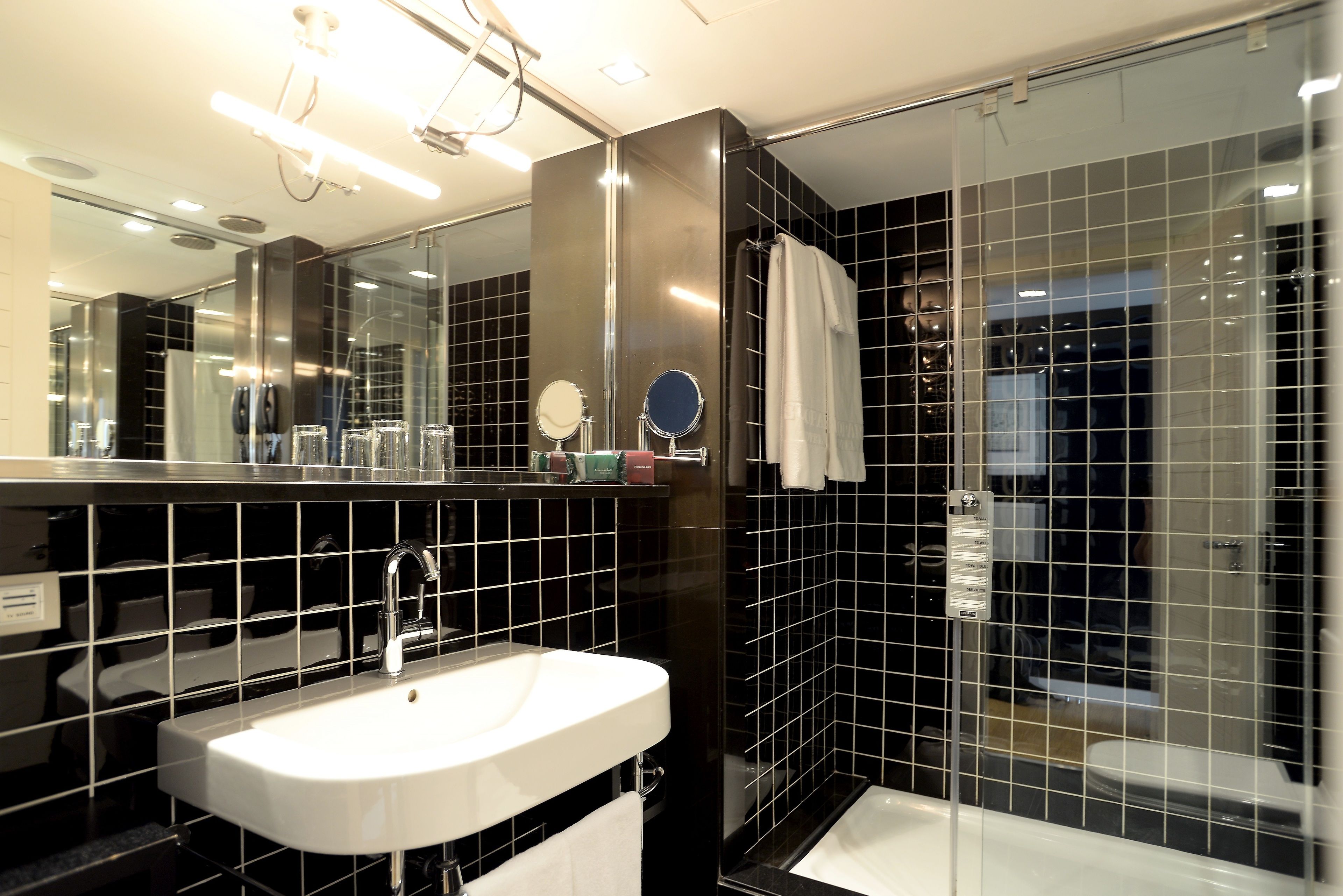 A modern bathroom with a white sink, black tiled walls, and a glass shower enclosure.