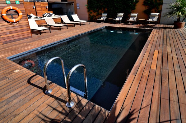 Zona de piscina con cubierta de madera, sillas de descanso y un flotador.