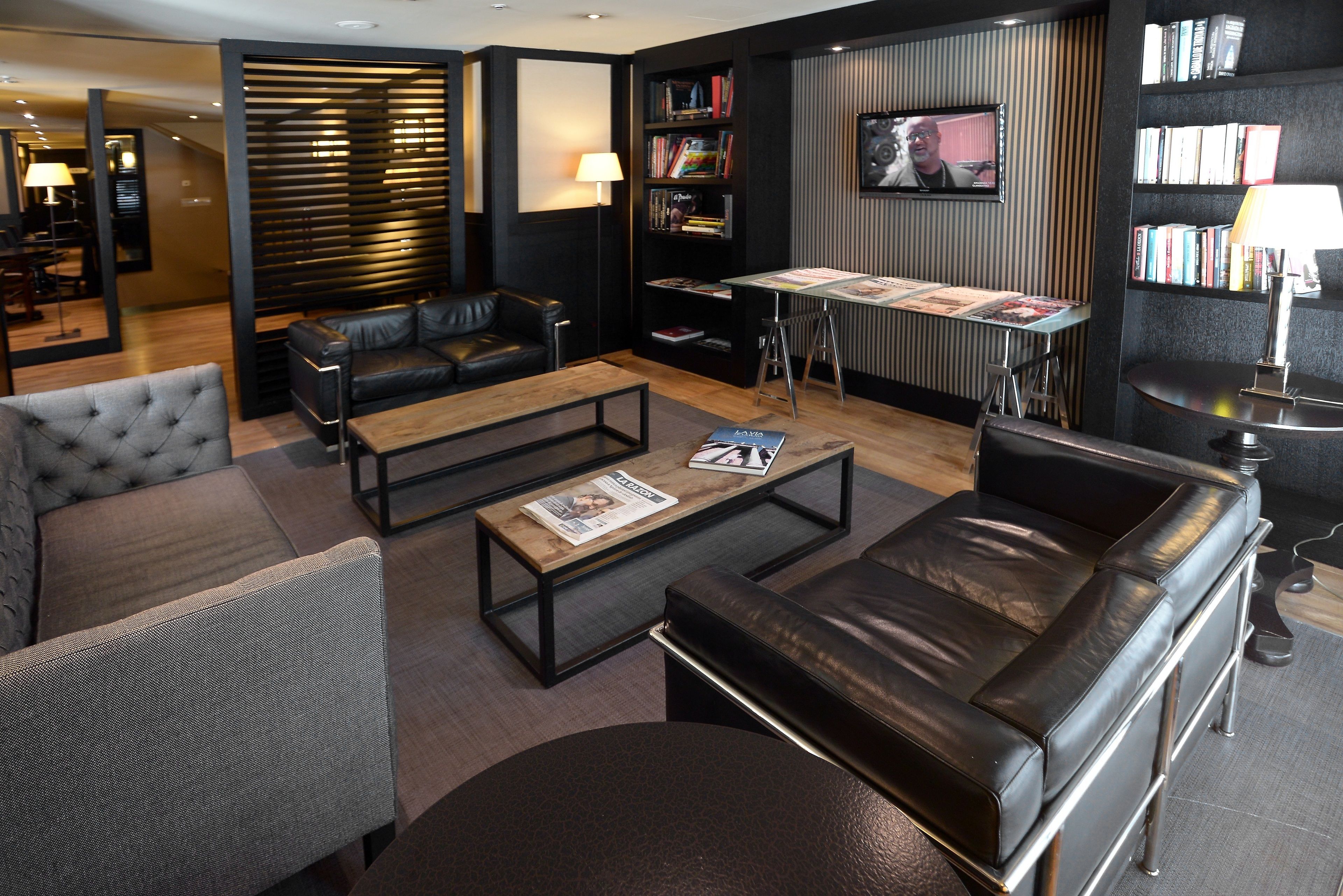 A modern living room with leather sofas, a coffee table, a bookshelf, and a TV mounted on the wall.