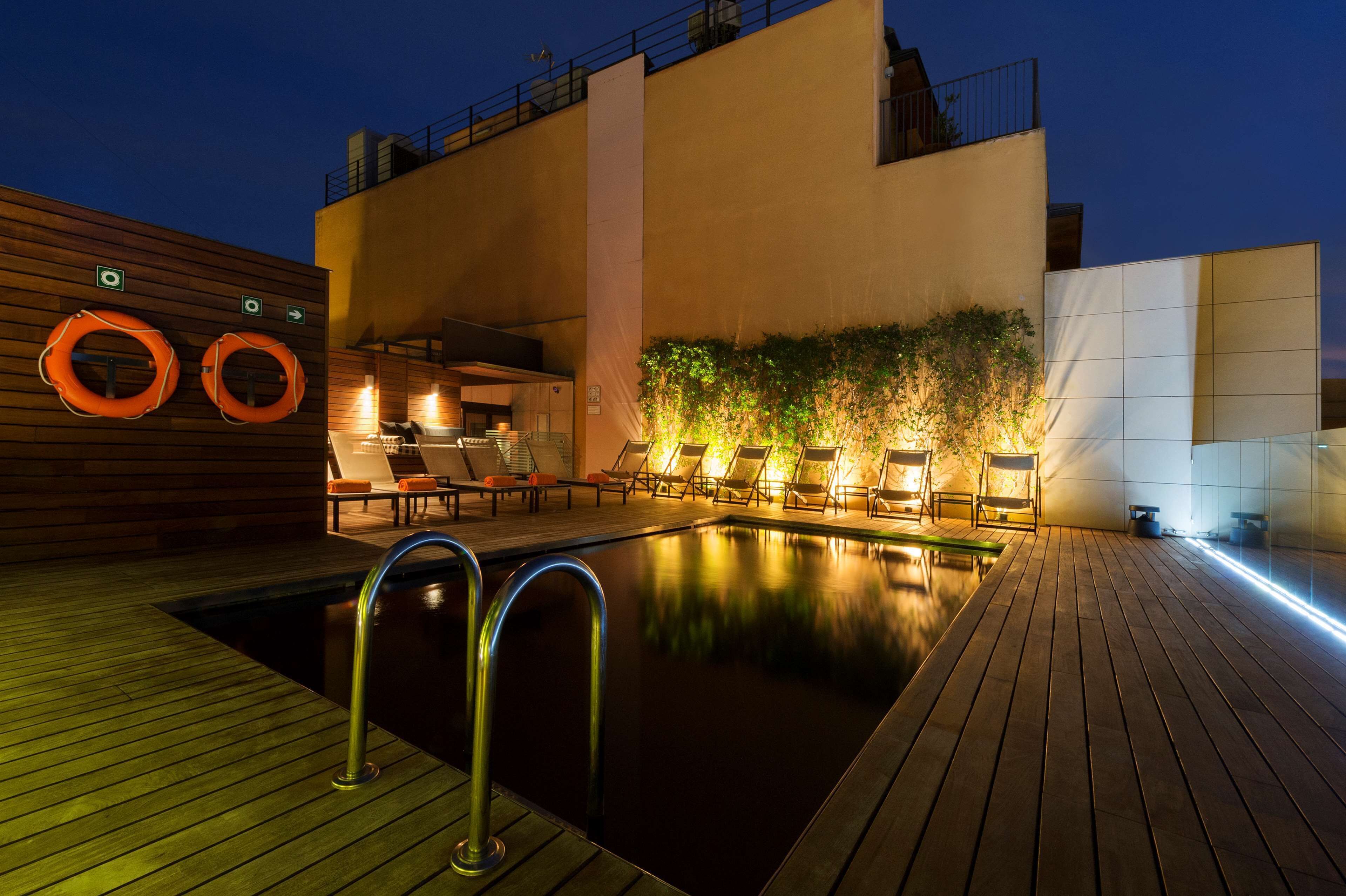 Un área de piscina en la azotea con terraza de madera, sillones de descanso y una pequeña zona de bar.
