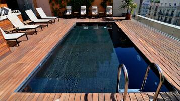 Una piscina en la azotea con cubierta de madera, sillones de descanso y plantas en macetas.