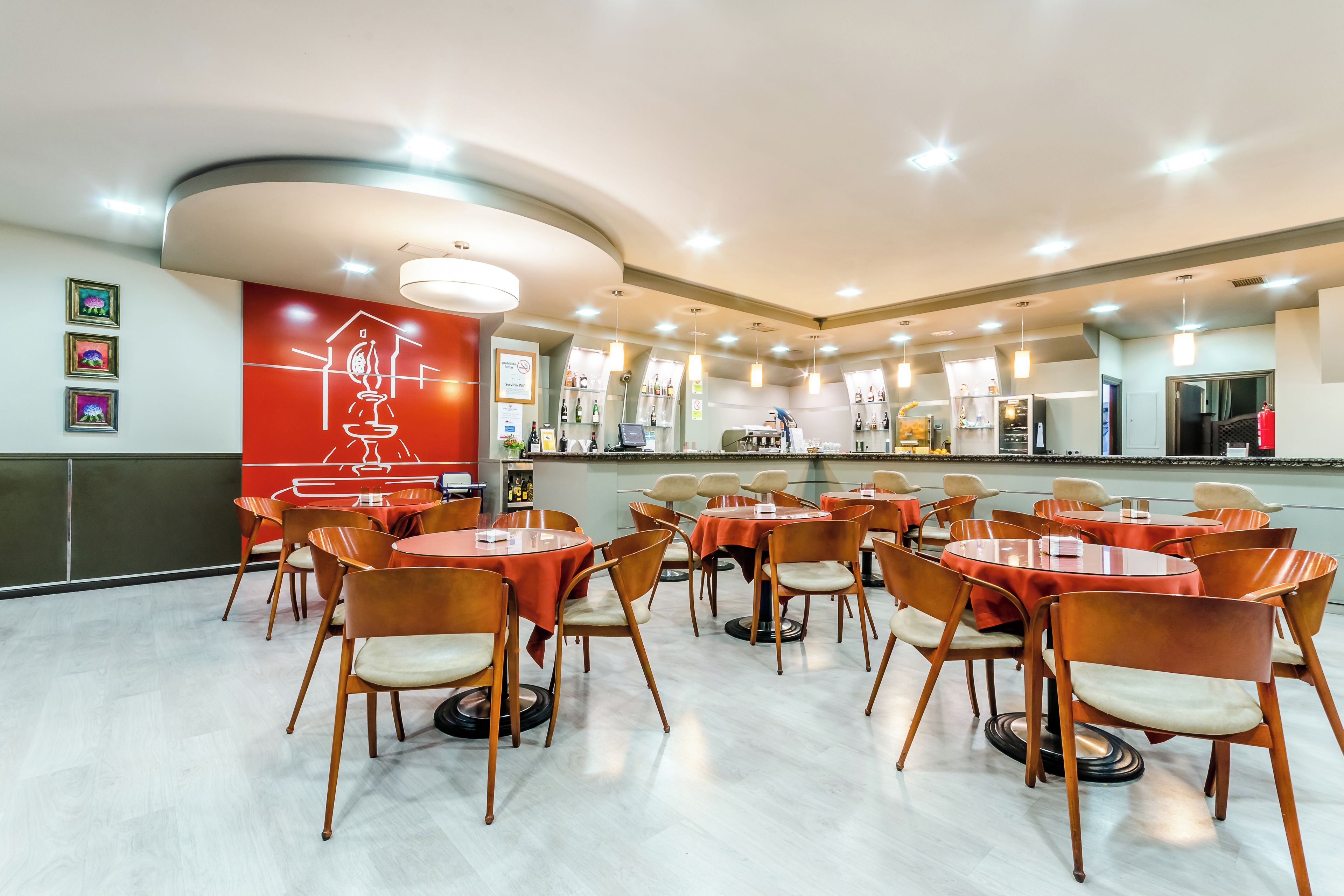 Un restaurante con mesas y sillas redondas, una barra con un menú y una pared con obras de arte enmarcadas.
