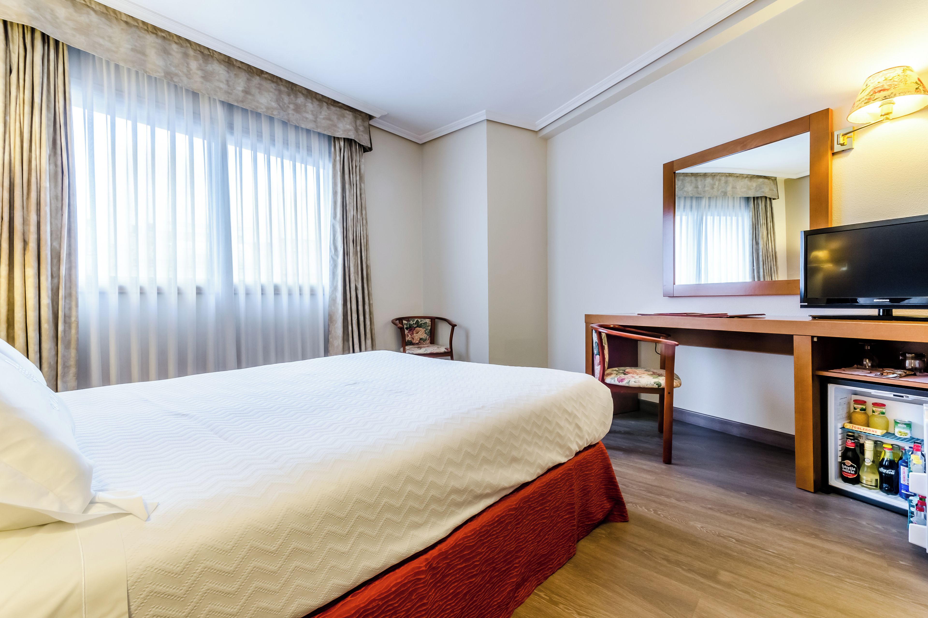 Ein Hotelzimmer mit einem Bett, einem Schreibtisch, einem Sessel, einem Fernseher und einer Minibar.