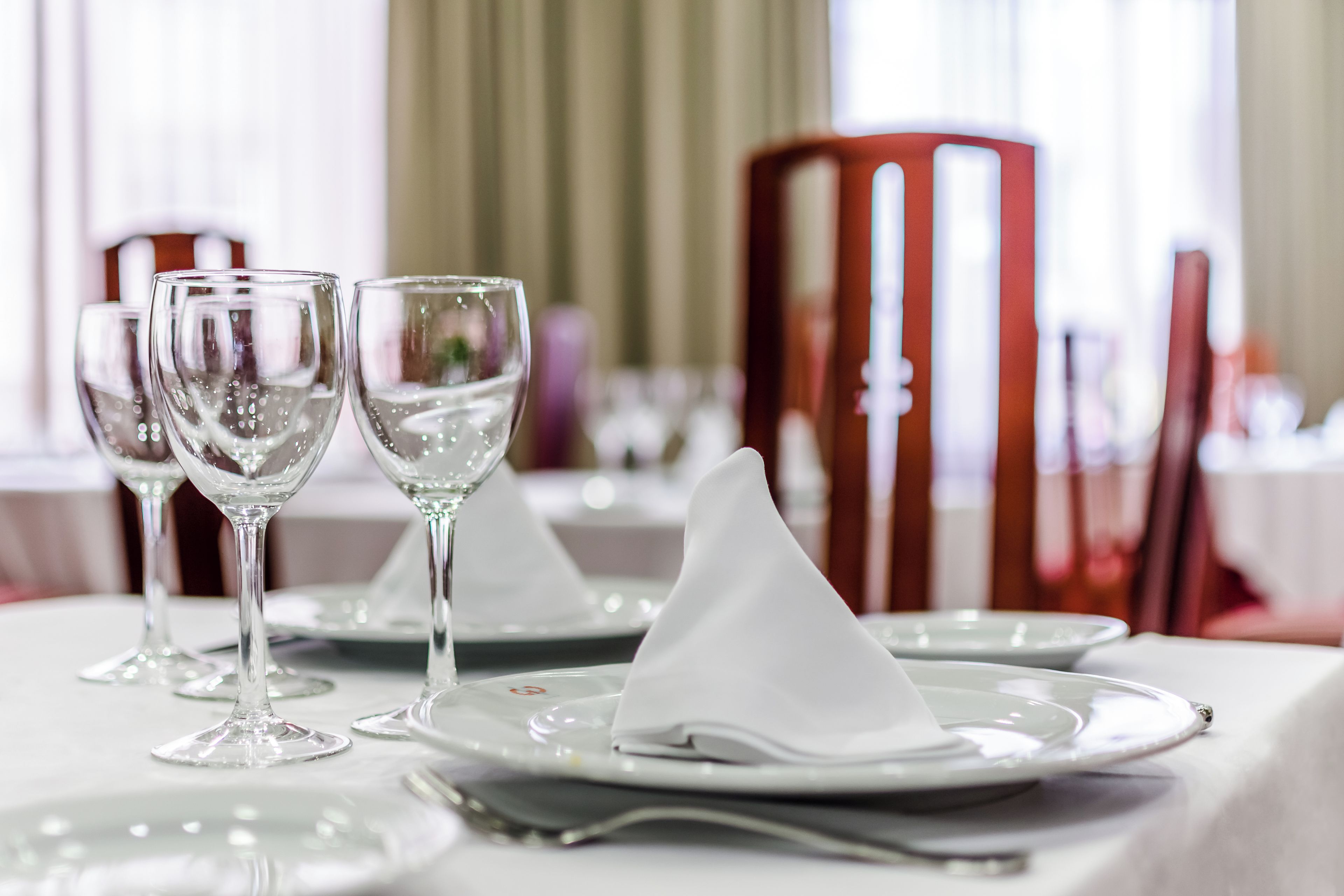 A table set with clear glassware and white napkins, with a red chair in the background.