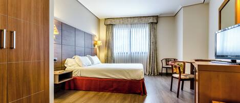 Quarto de hotel com uma cama, uma escrivaninha com televisão, uma cadeira e um guarda-roupa.