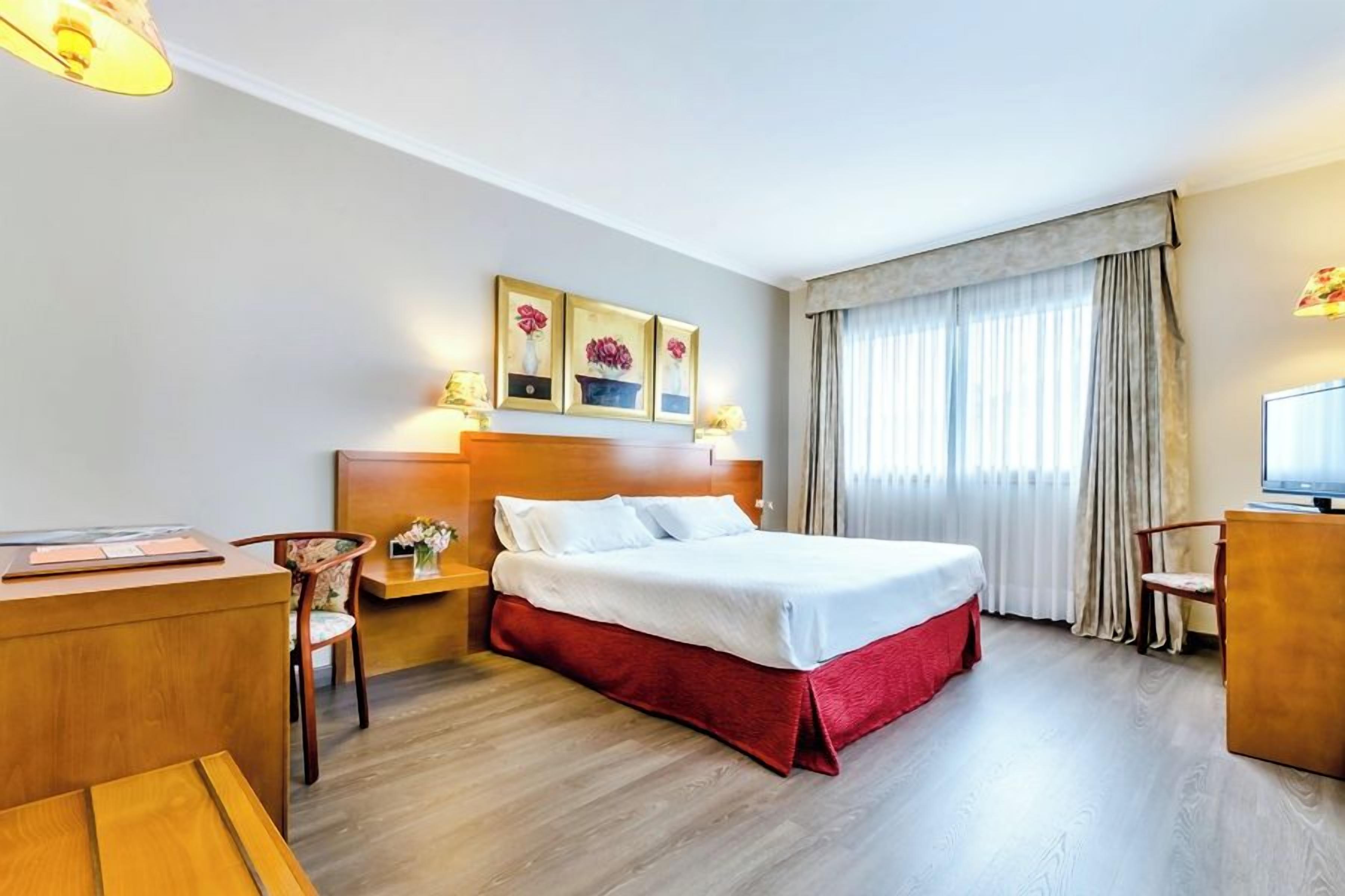 A hotel room with a bed, desk, chair, and a television.
