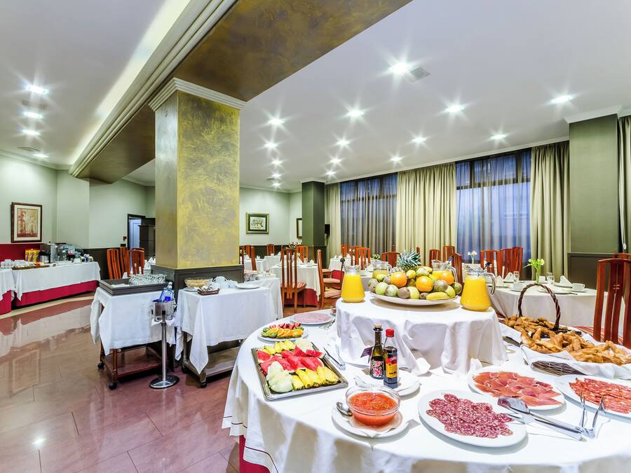 A buffet setup with various food items and beverages, tables with white tablecloths, and a room with a high ceiling and recessed lighting.