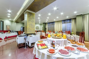 Montaje tipo bufé con diferentes alimentos y bebidas, mesas con manteles blancos, y una sala con techo alto e iluminación empotrada.