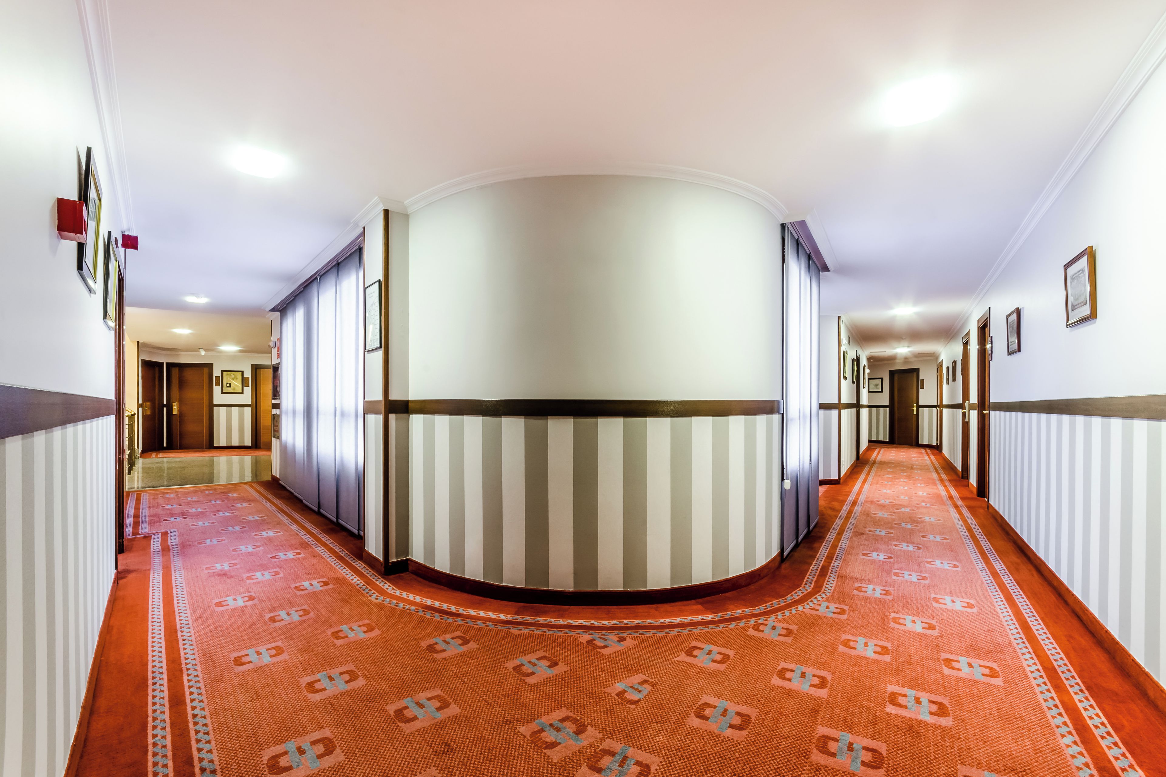 A hotel corridor with a curved wall, striped wallpaper, and a patterned carpet.