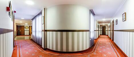 A hotel corridor with a curved wall, striped wallpaper, and a patterned carpet.