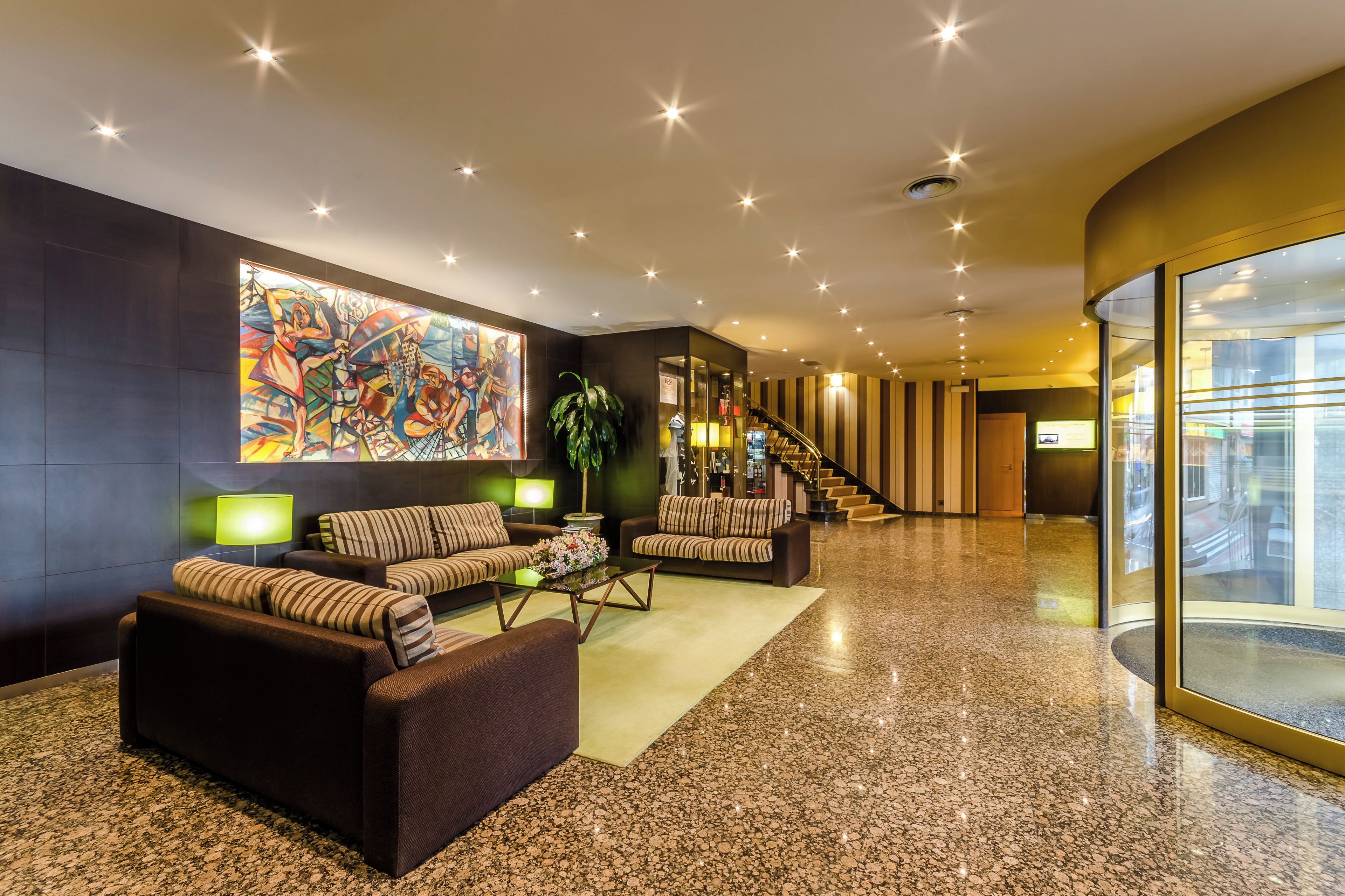 A modern lobby with a large abstract painting, multiple sofas, a staircase, and a glass wall offering a view.