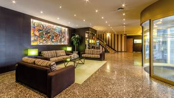 A modern lobby with a large abstract painting, multiple sofas, a staircase, and a glass wall offering a view.