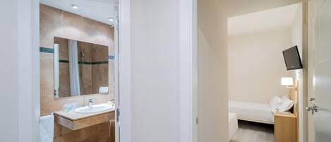 A hotel room with a bathroom, a bed, a TV, and a bedside table.
